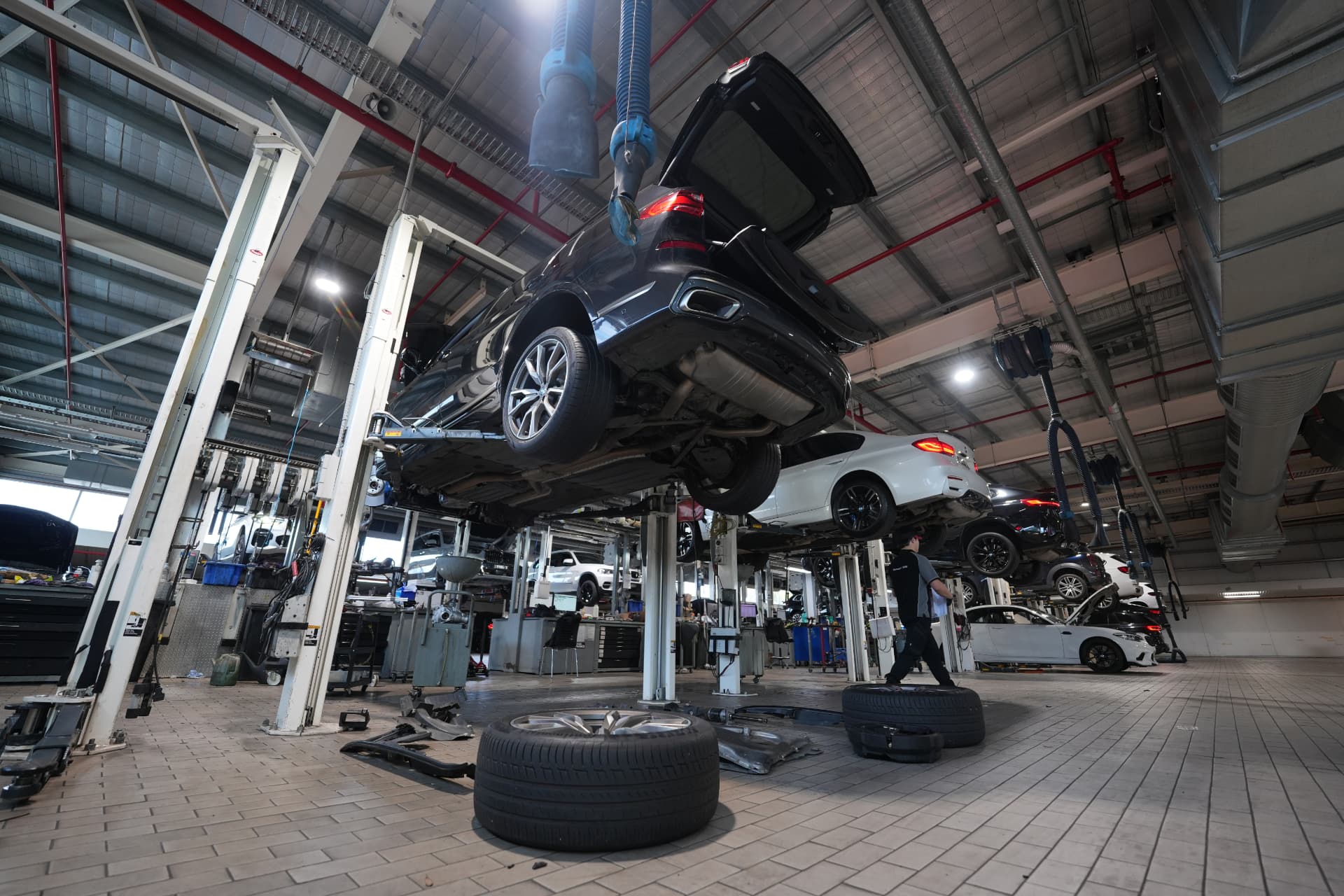 Workshop service bays with luxury vehicles raised on hydraulic hoists and blue exhaust extraction hoses overhead